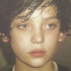 a close up of a young person wearing a necklace and looking at the camera with an intense look on his face