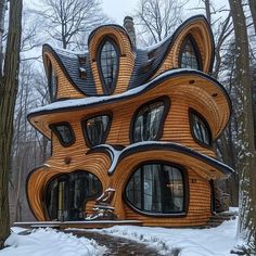 a house made out of wood in the woods with snow on the ground and trees around it