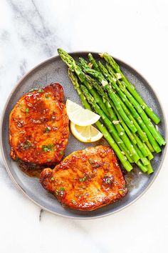 two pieces of chicken, asparagus and lemon wedges on a gray plate