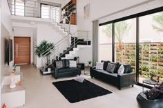 a living room filled with black furniture next to a stair case and glass door leading up to the second floor