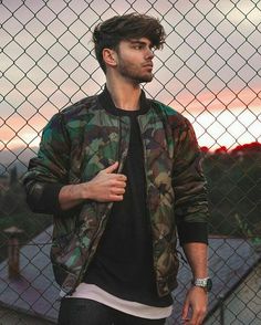 a young man standing in front of a chain link fence with his hand on his hip