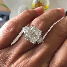 a woman's hand holding an engagement ring with a diamond in the middle and two diamonds on each side