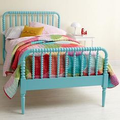 a blue bed with colorful pillows and blankets on it's headboard, in a white room