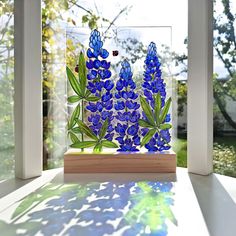 a glass vase with blue flowers in it sitting on a window sill