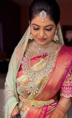 a woman in a pink and green sari with jewelry on her head, looking down at the camera