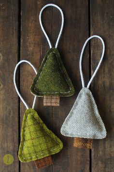 three small christmas trees hanging from strings on a wooden surface with white string and green fabric