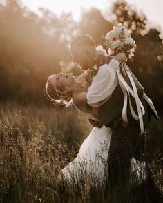 a man holding a woman in his arms while standing in the middle of a field