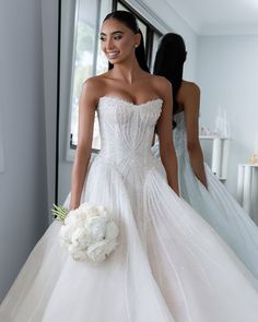 a woman in a white wedding dress holding a bouquet and looking at herself in the mirror