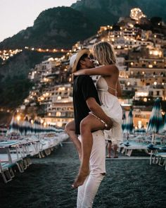 a man and woman are dancing in front of the ocean at night with lights on buildings behind them