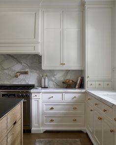 a kitchen with marble counter tops and white cabinets, along with brass pulls on the drawers