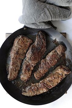 steaks are cooking in a skillet on the stove top next to an oven mitt