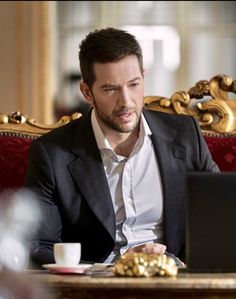 a man sitting in front of a laptop computer on top of a red couch next to a cup of coffee