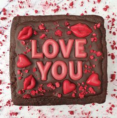 a chocolate cake with the words love you spelled in red frosting on top and hearts around it