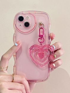 a person holding a pink phone case with a heart shaped keychain attached to it