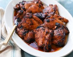 a white plate topped with chicken covered in bbq sauce next to a wooden spoon