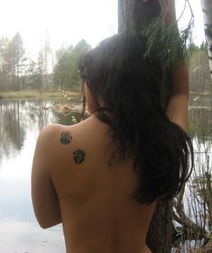 a woman with tattoos on her back standing next to a lake