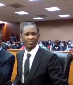 two men in suits sitting next to each other at a table with people behind them