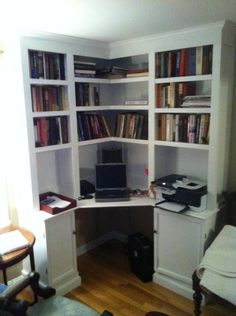 a computer desk sitting in the corner of a room with lots of bookshelves