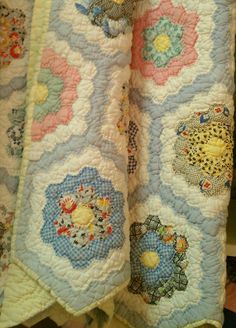 two quilted bedspreads with flowers and birds on them are hanging from a rack