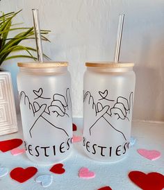 two personalized glass tumblers with straws and hearts on the table next to a potted plant