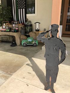 a statue of a man holding a baseball bat next to a green car and american flag