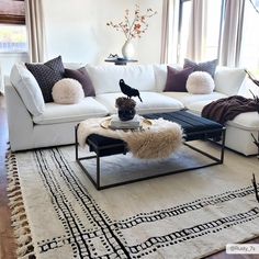 a living room with white couches and pillows on top of the rugs in front of large windows