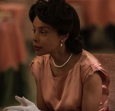 a woman sitting in a chair wearing white gloves and pearls on her head, looking off to the side