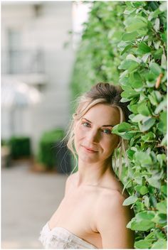 a woman standing next to a green bush