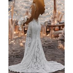 a woman in a wedding dress is standing on the beach with her back to the camera