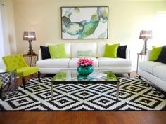 a living room with white couches and green accent pillows on top of the rug