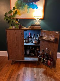 a cabinet with liquor bottles and glasses in it on the floor next to a painting