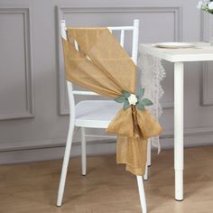 a chair with a bow on it next to a white table and flowers in vase