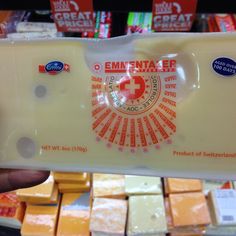 a person holding up a piece of cheese in front of other cheeses on display