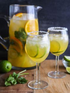 two glasses filled with lemonade and limes on top of a wooden table