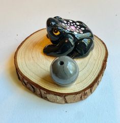 a frog figurine sitting on top of a piece of wood next to a ball