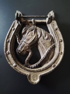 a metal horse head mounted to the side of a door knocker on a black wall