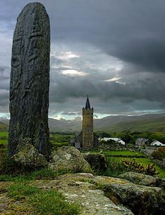 a large stone standing in the middle of a lush green field next to a tall rock