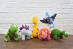 knitted toy dinosaurs lined up in front of a white brick wall with one dinosaur facing the camera