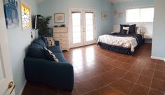 a bedroom with blue walls and tile flooring has a bed, couch, and dresser in it