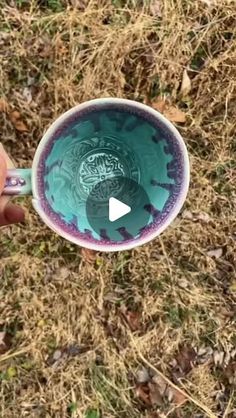 someone is holding a cup with blue and purple designs on it in the grass,