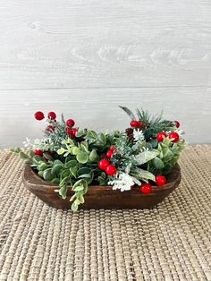 a wooden bowl filled with greenery and red berries