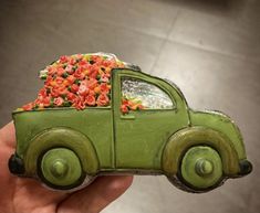 a hand holding a green toy truck with flowers in the bed and on top of it