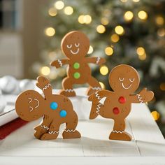 three gingerbread cutouts sitting on top of a table next to a christmas tree