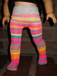 the doll is wearing colorful leggings and has her hands in her pockets as she stands next to a brick wall