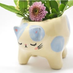 a ceramic cat planter with purple flowers in it's mouth and eyes painted on