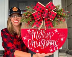 a woman holding up a merry christmas heart shaped door hanger with the words merry christmas on it