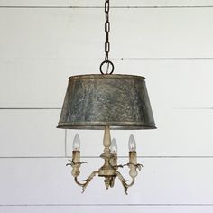 an old fashioned chandelier hanging from a chain on a white wall with wood planks