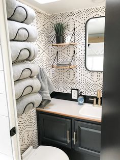 a white toilet sitting next to a bathroom sink under a mirror on top of a wooden shelf