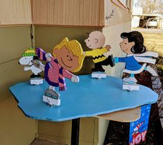 peanuts on skateboards are playing with each other in front of a blue table outside