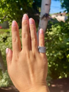 a woman's hand with a diamond ring on top of her finger and trees in the background